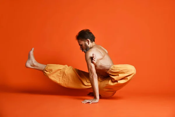 Viejo practicando yoga haciendo ejercicios de estiramiento sobre fondo naranja — Foto de Stock