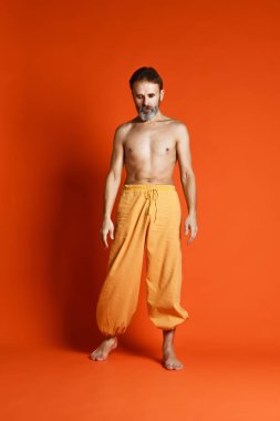 Turuncu arka planı germe yapıyor yaşlı adam pratik yoga egzersizleri