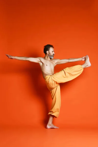 Vecchio che pratica yoga facendo esercizi di stretching contro sfondo arancione — Foto Stock