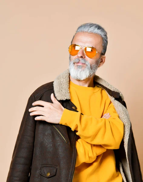 Портрет дорослого чоловіка з бородою і вусами в шкіряному пальто і береті, суворий вигляд, студія на коричнево-блакитному фоні — стокове фото