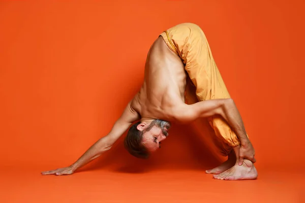 Viejo practicando yoga haciendo ejercicios de estiramiento sobre fondo naranja — Foto de Stock