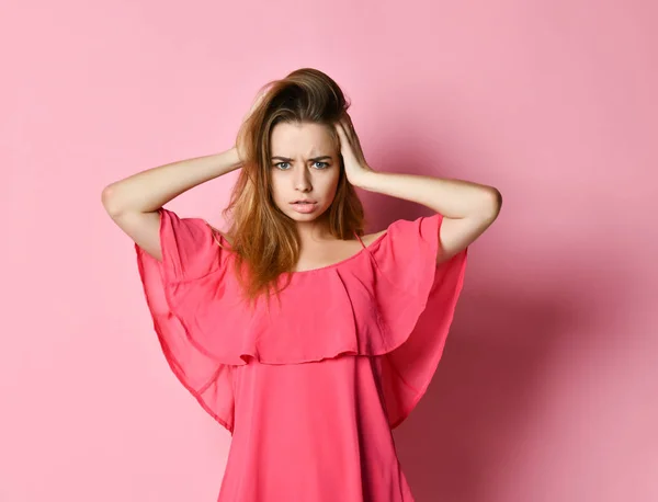 Mujer joven con cabello rubio en vestido rosa frunciendo el ceño agarrando la cabeza — Foto de Stock