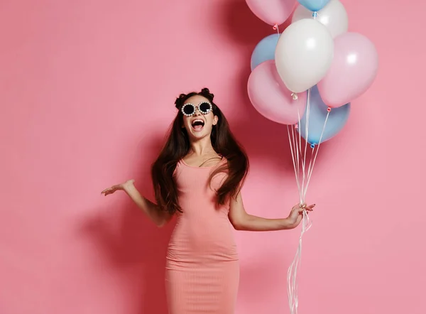 Yaygın olarak gülümseyen ve mavi ve pembe baloons ile oynarken bir stüdyoda şirin sarışın kız ayakta Close-up.