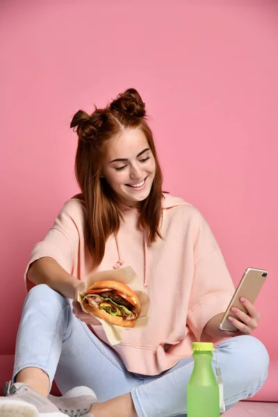 Hamburger yeme ve seyir telefon kız. Gençlik hayatı kavramı — Stok fotoğraf