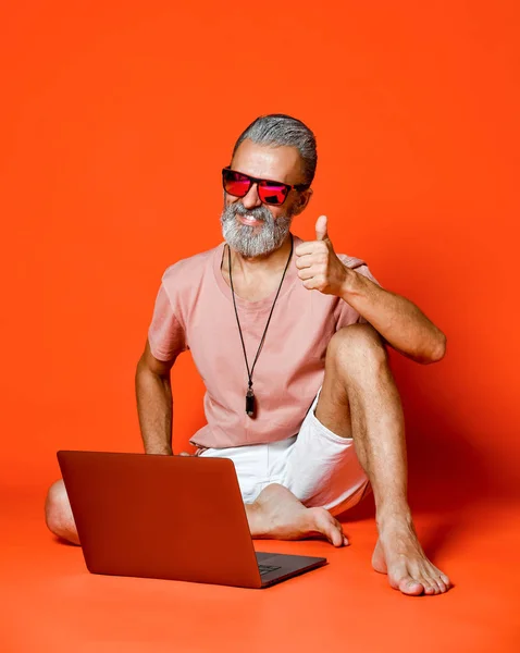 Retrato de cuerpo entero de un anciano feliz usando ordenador portátil aislado sobre fondo naranja — Foto de Stock