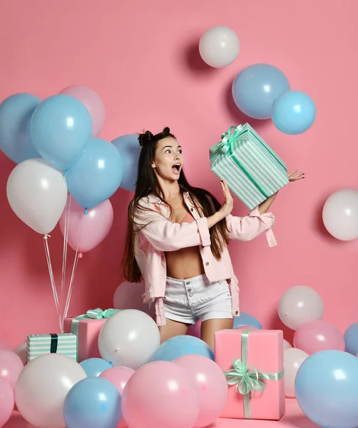 stock image Portrait of young woman in birthday party holding gift box with gift present on pastel pink background with colorful air baloons.