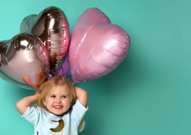 Küçük kız, kalp şeklinde pembe hava balonlarıyla eğleniyor..