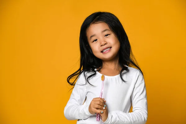 Portrait d'une petite fille tenant une brosse à dents sur fond jaune — Photo