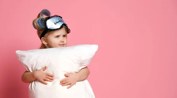 Портрет маленькой блондинки в пижаме и масках для глаз, стоящей с подушкой в руках — стоковое фото