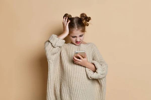 Beautiful blond little girl looks at the phone confusedly, isolated studio photo on the background — Stock Photo, Image