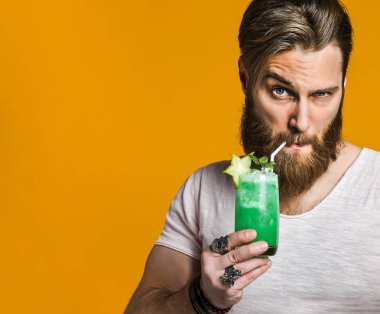 Genç adam elinde renkli bir kokteyl tutuyor.