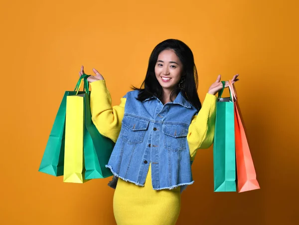Молодая азиатка с пакетами для покупок на цветном фоне — стоковое фото