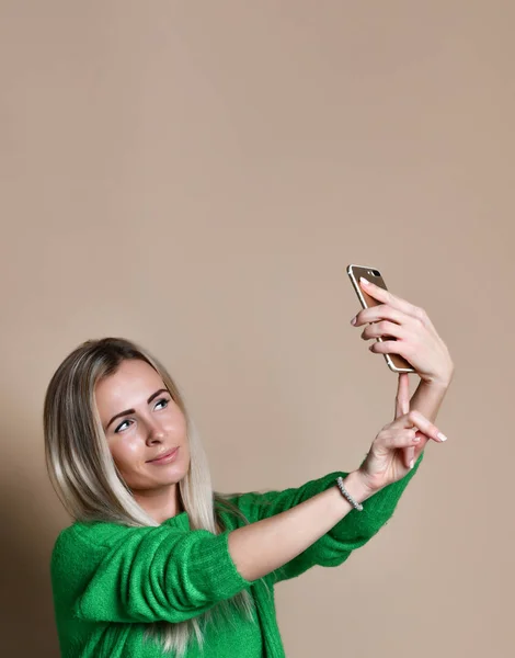 Retrato de cerca de la joven mujer rubia de moda alegre en ropa de jersey hace selfie en el teléfono inteligente, sobre fondo beige — Foto de Stock