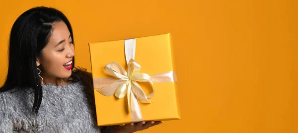 노란 배경 위로 열려져 있는 선물 상자를 들고 미소짓고 있는 예쁜 소녀의 모습 — 스톡 사진