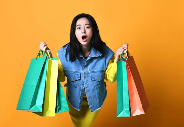 Jeune femme asiatique avec des sacs à provisions sur fond de couleur — Photo