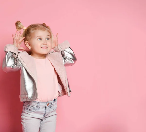 Retrato de una niña mirando a un lado del marco y mostrando bromas sobre un fondo rosa — Foto de Stock