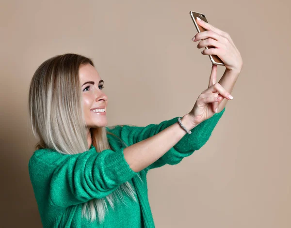 Retrato de cerca de la joven mujer rubia de moda alegre en ropa de jersey hace selfie en el teléfono inteligente, sobre fondo beige — Foto de Stock