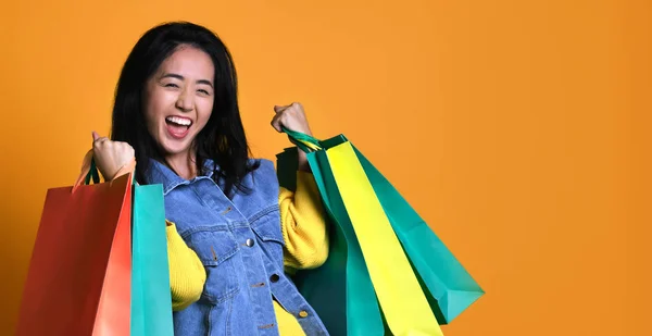Молодая азиатка с пакетами для покупок на цветном фоне — стоковое фото
