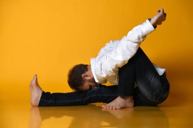 Yaşlı adam resmi ofis kıyafetleriyle yoga yapıyor. Sarı arka planda izole edilmiş..