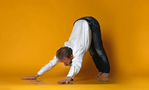 Viejo practicando yoga haciendo ejercicios de estiramiento sobre fondo amarillo — Foto de Stock