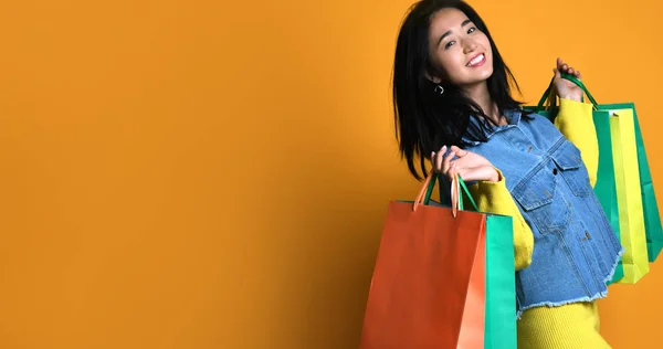 Jonge aziatische vrouw met boodschappentassen op kleur achtergrond — Stockfoto