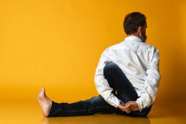 Yaşlı adam resmi ofis kıyafetleriyle yoga yapıyor. Sarı arka planda izole edilmiş..