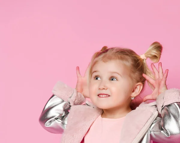 Portret van een klein meisje dat naar de zijkant van het frame kijkt en teasers op een roze achtergrond laat zien — Stockfoto