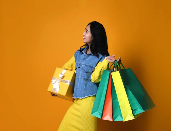 Jonge aziatische vrouw met boodschappentassen op kleur achtergrond — Stockfoto