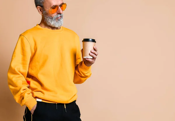 Fotografía vertical de un jubiloso anciano sosteniendo una taza de café blanco y mirando a la cámara — Foto de Stock