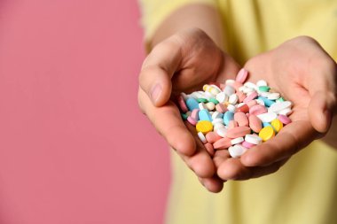 Pembe arka planda tişörtlü yakışıklı bir adam elinde haplar tutuyor.