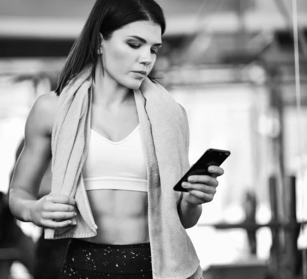 Mladé, fit žena pomocí smartphone v tělocvičně — Stock fotografie