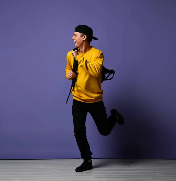 Χαρούμενος νέος μαθητής με ένα σακίδιο τρέχει απομονώνεται σε στούντιο σε μωβ φόντο — Φωτογραφία Αρχείου