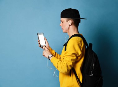 Şapkalı, gözlüklü ve mor arka planda akıllı telefon kullanan neşeli bir öğrencinin portresi.