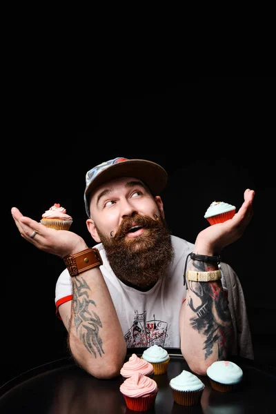 Happy bearded bald man holding two cream cakes on black background.