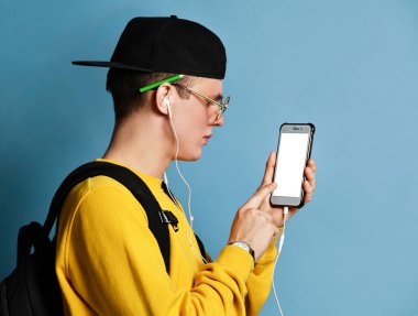 Şapkalı, gözlüklü ve mor arka planda akıllı telefon kullanan neşeli bir öğrencinin portresi.