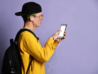 Şapkalı, gözlüklü ve mor arka planda akıllı telefon kullanan neşeli bir öğrencinin portresi.