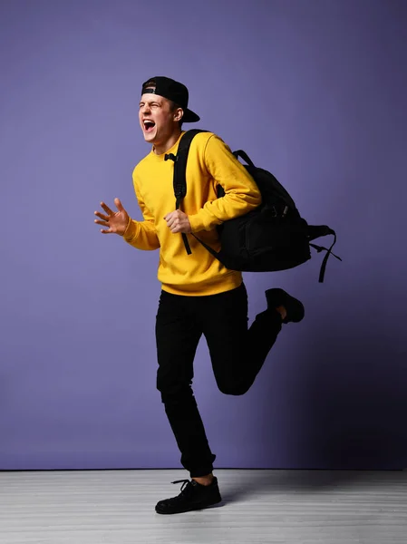 Joyful jovem estudante com uma mochila corre isolado em estúdio em um fundo roxo — Fotografia de Stock