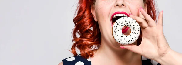 Portrait of beautiful cheerful fat plus size woman pin-up wearing a polka-dot dress isolated over light background, eating a donut — Stock Photo, Image