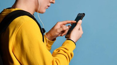 Şapkalı, gözlüklü ve mor arka planda akıllı telefon kullanan neşeli bir öğrencinin portresi.