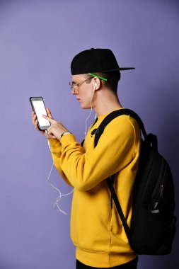 Şapkalı, gözlüklü ve mor arka planda akıllı telefon kullanan neşeli bir öğrencinin portresi.