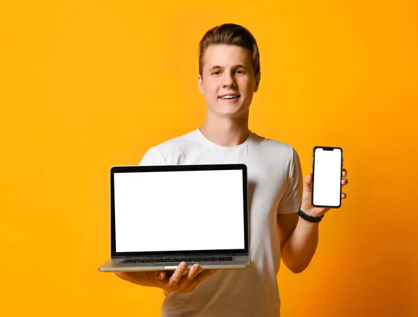 Giovane studente in camicia bianca, in possesso di un computer portatile e smartphone mobile, in piedi mostra lo schermo del telefono e del computer nella cornice. — Foto Stock