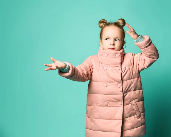 Linda niña en un abrigo de primavera apunta con dos palmas de sus manos a un lado para liberar espacio. — Foto de Stock