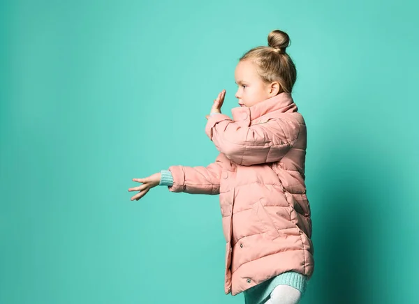 Linda niña en un abrigo de primavera apunta con dos palmas de sus manos a un lado para liberar espacio. — Foto de Stock