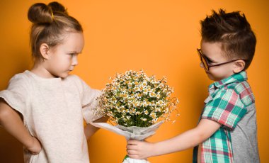 little boy gives a bouquet of daisies to his girlfriend a girl. The girl angrily folded her arms in front of her and did not want to take a gift. Concept of friendship, quarrel, date clipart