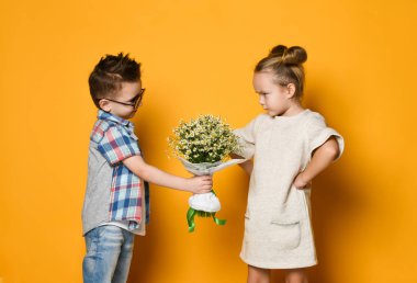 Mutlu beyaz çocuk sarı arka planda izole edilmiş kız arkadaşına çiçek veriyor..