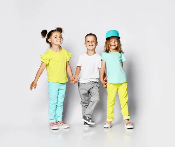 Studio portrait of children on a light background: full body shot of three children in bright clothes, two girls and one boy. Triplets, brother and sisters. — Stock Photo, Image