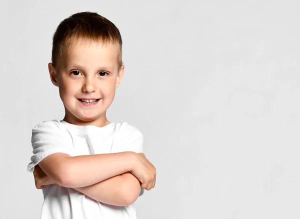 Piękny chłopiec w białej koszulce, trzymający skrzyżowane i uśmiechnięte ramiona, stojący na białym tle — Zdjęcie stockowe