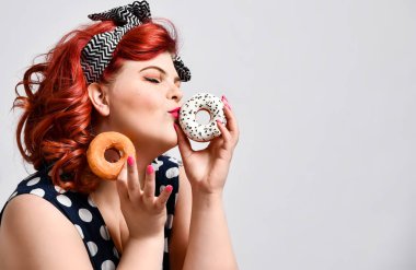 Güzel, neşeli, şişman kadın portresi. Puantiyeli bir elbise giyiyor. Arka planda izole edilmiş, çörek yiyor.