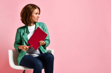 Genç bir kadın sandalyede not defteriyle ders çalışıyor.