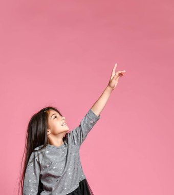 pembe bir arka plan üzerinde duran küçük kız elini kaldırdı, bir yere işaret.
